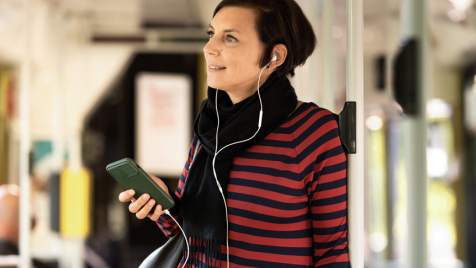 Frau steht mit Handy in der Hand in der Straßenbahn